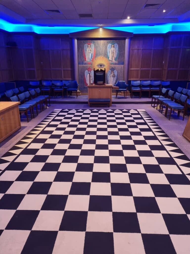 The interior of a freemason lodge, chequered floor with chair aligned around a central dais.